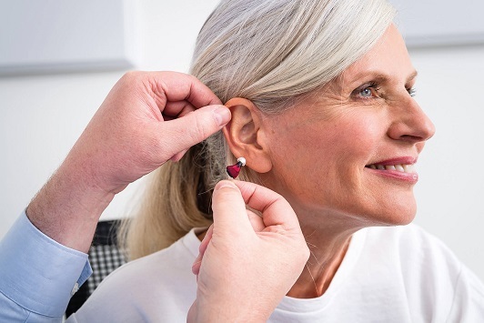 Ältere Frau bekommt ein modernes Hörgerät, Hörakustiker passt Hörhilfe am Ohr an.